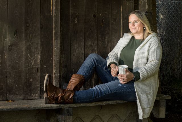 Nicole Gansner sitzt mit einer Tasse Tee auf einer Holzbank