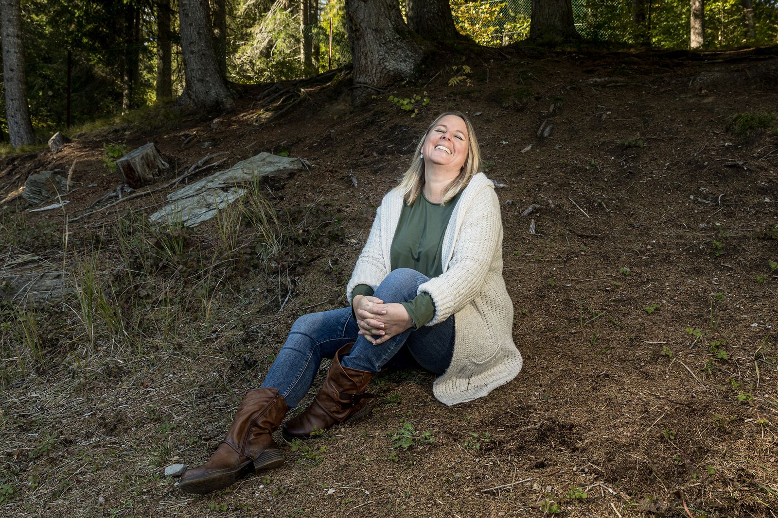 Nicole Gansner sitzt lachend auf dem Waldboden im Prättigau, Graubünden